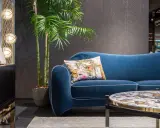 Divano blu petrolio con cuscino decorato. Abbinamenti eleganti con tavolino e arredi moderni.