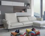 Un divano bianco in pelle, con cuscini colorati sparsi sul tappeto, davanti a una finestra con vista sulla città al tramonto. L'alba calia illumina la scena.