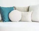 Cuscini di varie forme e colori su un divano bianco. Scopri come lavare i cuscini del divano per mantenerli freschi e puliti.