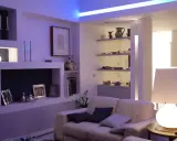 Soggiorno moderno con illuminazione soffusa, ideale per come illuminare un soggiorno con poca luce. Divano bianco, mensole con oggetti e lampada da tavolo.