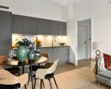 Arredare una sala moderna con cucina a vista: tavolo rotondo con sedie in legno, vasi verdi e candele.