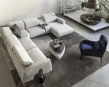 Ampio soggiorno con un grande divano modulare di colore chiaro, un tappeto scuro e un pavimento chiaro. Un poltrona blu e un tavolino completano l'arredo.
