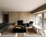 Elegante salone moderno con divani scuri, camino a parete in legno, tavolino nero e poltrona. Un esempio di come arredare un salone con stile minimalista.