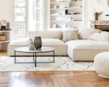 Un soggiorno luminoso con divani e design moderno. Un divano componibile bianco, una poltrona bouclé e una sedia grigia su un tappeto geometrico.