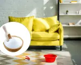 Un divano giallo brillante pronto per essere pulito con bicarbonato. Una ciotola di bicarbonato con un mestolo è in primo piano.