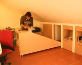 Uomo in mansarda con idee sottotetto molto basso: scrivania angolare, armadi a muro e sedia rossa.