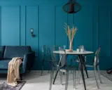 Soggiorno moderno con divano blu, tavolo rotondo con sedie trasparenti e pareti color ottanio.