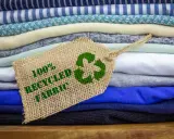 Pile di tessuti ecologici colorati, con un'etichetta che indica "100% Recycled Fabric" e il simbolo del riciclo.