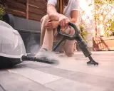 Persona usa un vaporetto per pulire la moquette esterna, creando una nuvola di vapore.