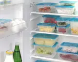 Frigo organizzato con contenitori trasparenti: carote, formaggio, cetrioli, uva, affettati. Un esempio di come organizzare il frigo per conservare al meglio gli alimenti.