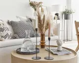 Un accogliente salotto bohemien con cuscini decorativi, un vaso di erba della pampa e candele su un tavolino rotondo.