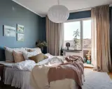 Accogliente camera da letto blu e beige con letto comodo, quadri astratti e grande finestra luminosa.