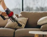 Mano che usa un aspirapolvere senza fili per pulire un divano in tessuto. Un modo semplice per capire come pulire divano in tessuto con folletto.