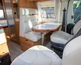Interno camper con sedili e divanetti in ecopelle o similpelle bianca, tavolo e finiture in legno.