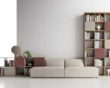 Un comodo divano beige è posizionato davanti a una libreria modulare in legno, con libri e oggetti decorativi.