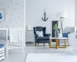 Un accogliente salotto stile marinaro con culla, poltrona blu e decorazioni a tema nautico.