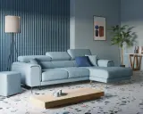 Accogliente soggiorno con divano angolare azzurro, tavolino in legno, lampada da terra e pianta.