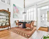 Soggiorno con arredamento misto moderno e antico: vetrina in legno intarsiato, tavolo scuro con sedie in pelle, tappeto persiano e quadro astratto.