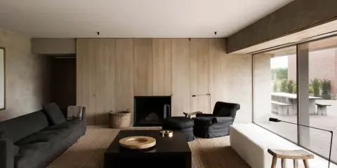 Elegante salone moderno con divani scuri, camino a parete in legno, tavolino nero e poltrona. Un esempio di come arredare un salone con stile minimalista.
