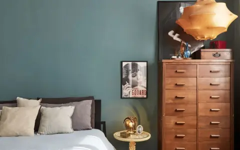 Un'elegante camera da letto con pareti color ottanio, un letto con cuscini in lino e un comò in legno. L'abbinamento colori camera da letto è sofisticato e rilassante.