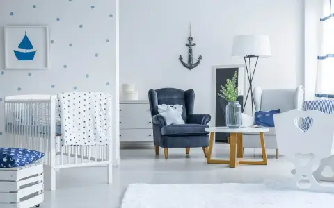 Un accogliente salotto stile marinaro con culla, poltrona blu e decorazioni a tema nautico.