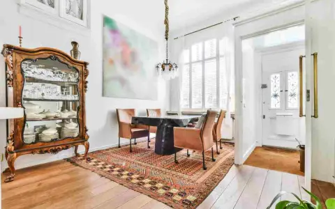 Soggiorno con arredamento misto moderno e antico: vetrina in legno intarsiato, tavolo scuro con sedie in pelle, tappeto persiano e quadro astratto.