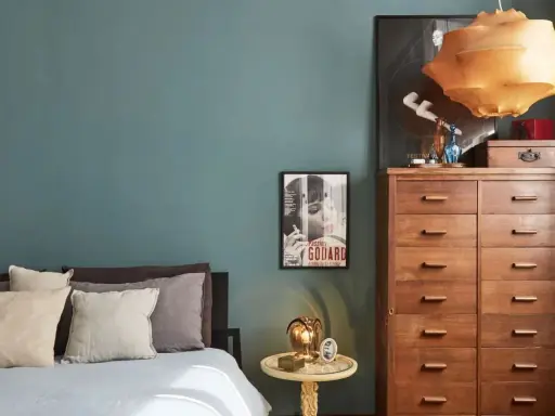 Un'elegante camera da letto con pareti color ottanio, un letto con cuscini in lino e un comò in legno. L'abbinamento colori camera da letto è sofisticato e rilassante.