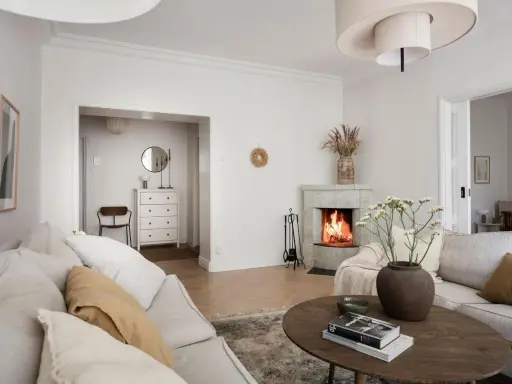 Accogliente soggiorno con camino acceso, divani chiari e un tavolino in legno. Idee per la casa e la campagna.