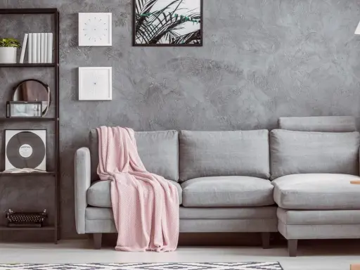 Un divano grigio con coperta rosa, una libreria nera con piante e vinile, e un tavolino di legno: ecco cosa mettere vicino al divano per un tocco di stile.
