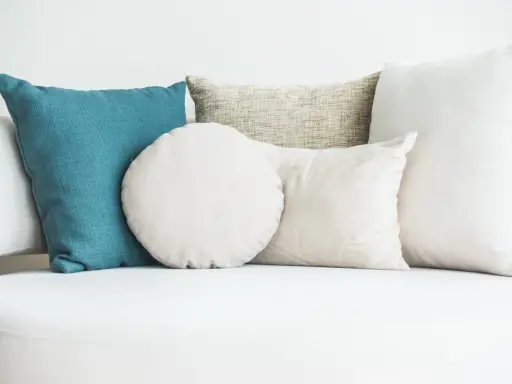 Cuscini di varie forme e colori su un divano bianco. Scopri come lavare i cuscini del divano per mantenerli freschi e puliti.