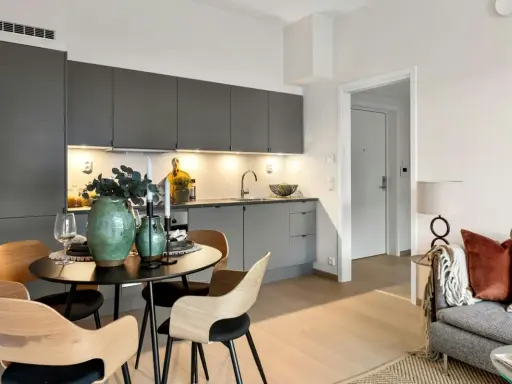Arredare una sala moderna con cucina a vista: tavolo rotondo con sedie in legno, vasi verdi e candele.
