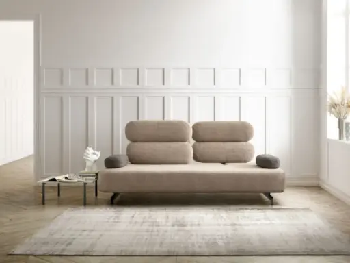 Un elegante divano beige, un'opera d'arte di design, domina la scena. Accanto, un tavolino con libri e una scultura moderna.