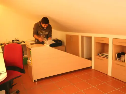 Uomo in mansarda con idee sottotetto molto basso: scrivania angolare, armadi a muro e sedia rossa.