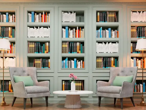 Libreria elegante con libri ordinati, poltrone comode e lampade. Un'ispirazione su come abbellire una libreria con stile e funzionalità.