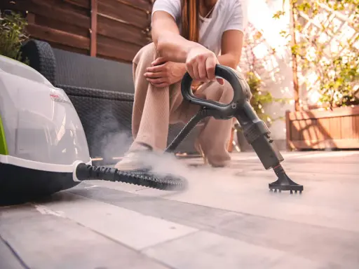 Persona usa un vaporetto per pulire la moquette esterna, creando una nuvola di vapore.