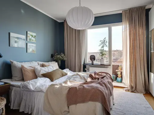 Accogliente camera da letto blu e beige con letto comodo, quadri astratti e grande finestra luminosa.