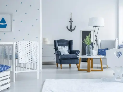 Un accogliente salotto stile marinaro con culla, poltrona blu e decorazioni a tema nautico.
