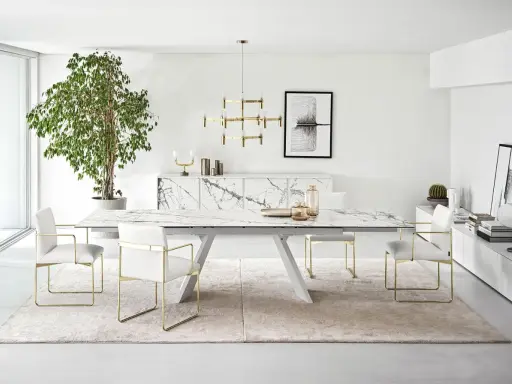 Un elegante soggiorno con un tavolo Calligaris in marmo, sedie bianche con dettagli dorati e un grande albero verde.