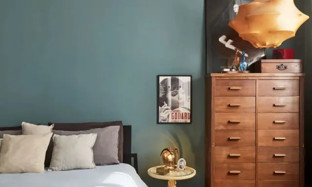 Un'elegante camera da letto con pareti color ottanio, un letto con cuscini in lino e un comò in legno. L'abbinamento colori camera da letto è sofisticato e rilassante.