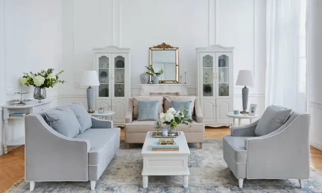 Elegante salotto shabby chic moderno con divani grigi, poltrone, tavolino bianco, specchio dorato e vetrine.