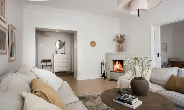 Accogliente soggiorno con camino acceso, divani chiari e un tavolino in legno. Idee per la casa e la campagna.