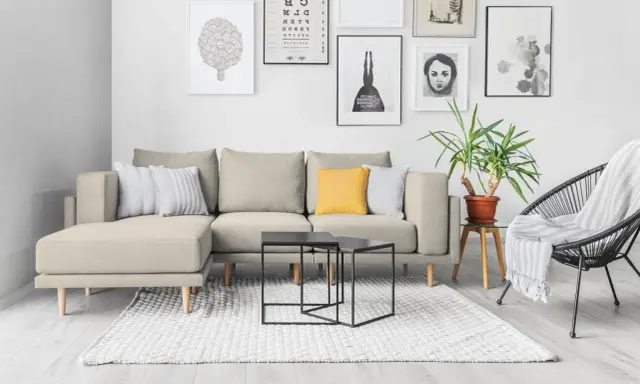 Divano componibile beige con cuscini, tavolini neri, tappeto bianco e sedia nera. Ispirazione per come foderare un divano fai da te.