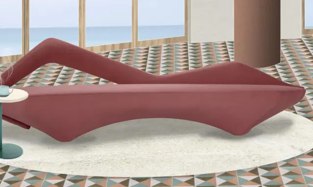 A pink velvet sofa with a unique curved design sits on a cream rug in a room with a geometric tiled floor and a view of the ocean.