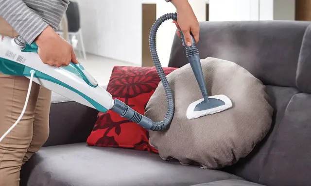 Persona pulisce un divano non sfoderabile con vaporetto, igienizzando i cuscini con vapore.