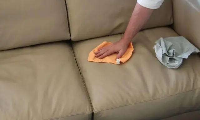 Mano che pulisce un divano in tessuto non sfoderabile con un panno arancione. Accanto, un panno grigio piegato.