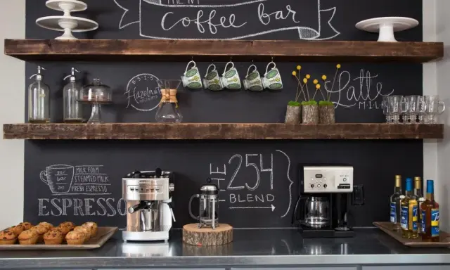 Un angolo caffè fai da te con macchine, tazze, muffin e scritte alla lavagna.