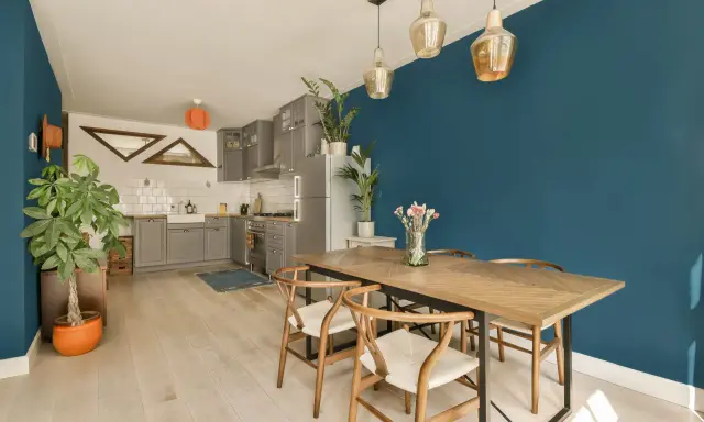 Un tavolo in legno con sedie in stile Wishbone, ideale per arredare sala da pranzo moderna. Parete blu intenso e cucina grigia completano l'ambiente.