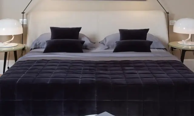 Un letto ben fatto, con copriletto trapuntato scuro e cuscini coordinati. Un esempio di come rifare il letto per un'atmosfera elegante.