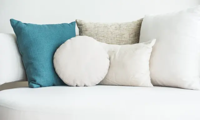 Cuscini di varie forme e colori su un divano bianco. Scopri come lavare i cuscini del divano per mantenerli freschi e puliti.