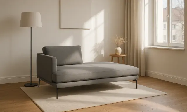 Chaise longue grigia moderna su tappeto chiaro, con lampada da terra e tavolino. Le misure sono perfette per un angolo relax.